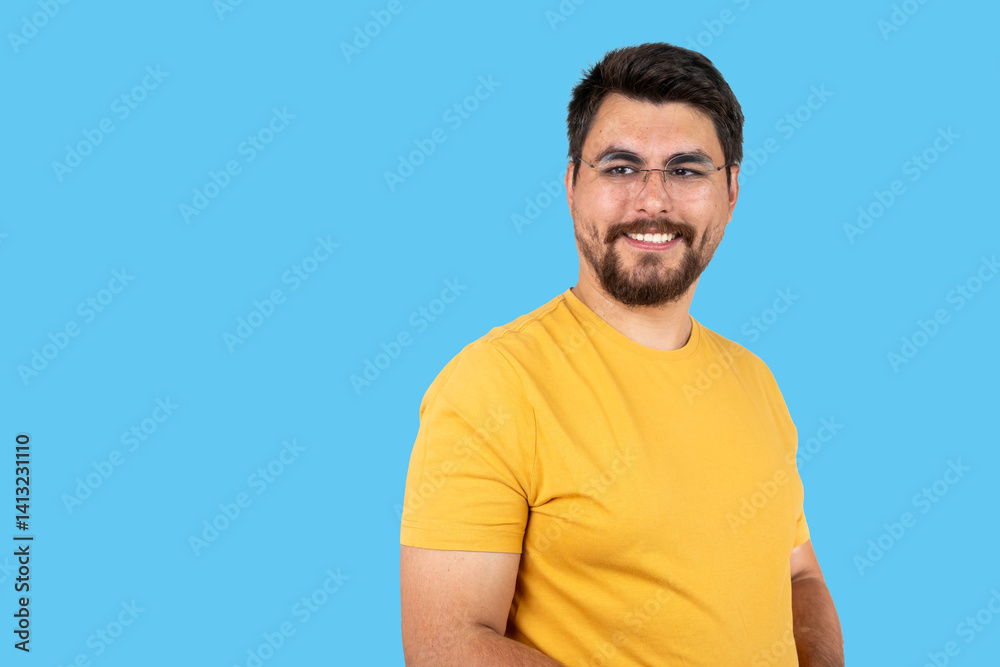 Obraz premium Indoor portrait of young european caucasian man isolated on blue background, standing in yellow t-shirt , smiling and looking straight at camera.