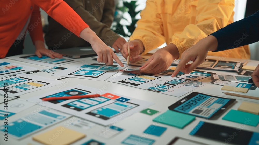 Obraz premium A diverse group of individuals collaborates on user interface mockups at a table filled with notes and tools, emphasizing teamwork in design and innovation. SACTR