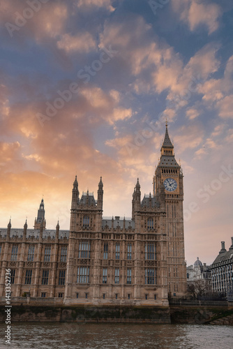 Obraz na płótnie Elizabeth Tower, part of the Palace of Westminster, stands against a sunset sky with orange and pink hues. The River Thames reflects the soft evening light. w salonie