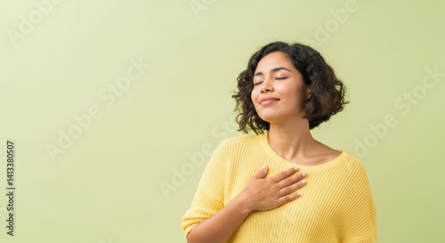 Young hispanic female embracing peace in yellow sweater against green background