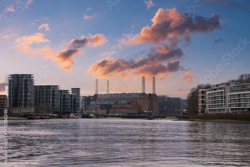 Obraz na płótnie Battersea Power Station with its four chimneys stands amid modern buildings. The River Thames flows in the foreground under a vibrant sunset sky. w salonie
