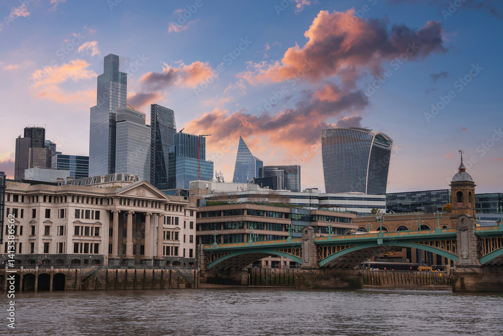 View of London's skyline featuring the Walkie Talkie and Gherkin buildings, Southwark Bridge over the River Thames, and a vibrant sunset sky.