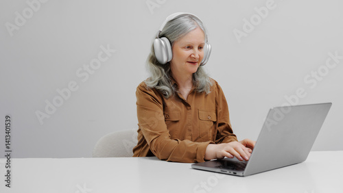 Woman using laptop while wearing headphones in a bright indoor setting during daytime
