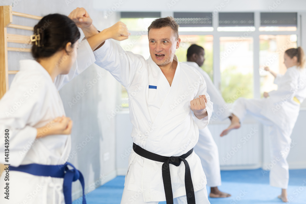 Fototapeta premium Adult man and young woman judokas practicing judo technique in group in gym