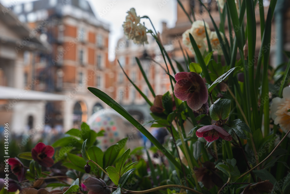 A colorful floral arrangement in the foreground contrasts with red brick buildings and arched windows in a lively urban London setting.