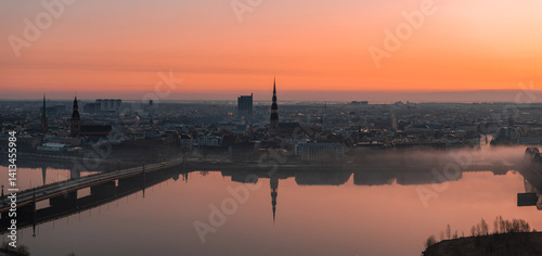 Obraz na płótnie Serene sunrise over Riga, Latvia, featuring St. Peter's Church spire, historic buildings, a bridge over the Daugava River, and light morning mist. w salonie