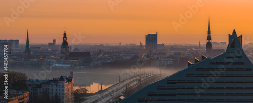 Obraz na płótnie Serene sunrise over Riga, Latvia, featuring St. Peter's Church, Riga Cathedral, the National Library, and a misty Daugava River with a bridge. w salonie