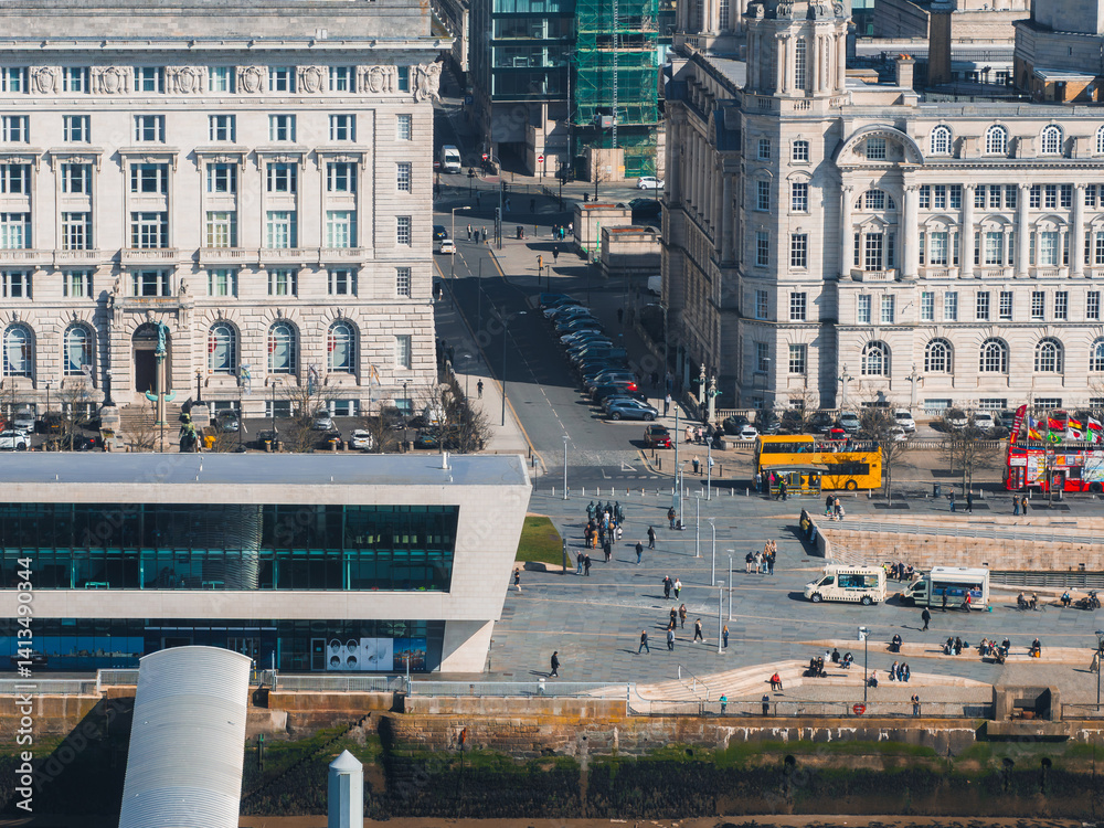 Aerial view of Liverpool showcasing the Three Graces, Museum of Liverpool, waterfront, and vibrant street activity with buses and pedestrians.