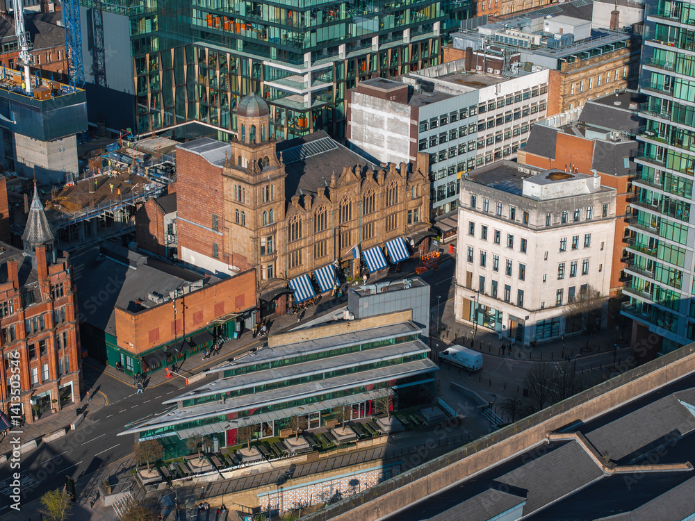Aerial view of Manchester city center, UK, showing a red brick domed landmark, glass skyscrapers, mid rise buildings, and a market with striped awnings.