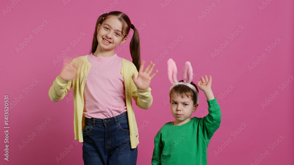 Joyful little kids waving in front of camera during easter holiday, smiling and wearing bunny ears. Brother and sister toddlers greeting someone in studio, adorable happy children. Camera B. Joyful little kids waving in front of camera during easter holiday, smiling and wearing bunny ears. Brother and sister toddlers greeting someone in studio, adorable happy children. Camera B.