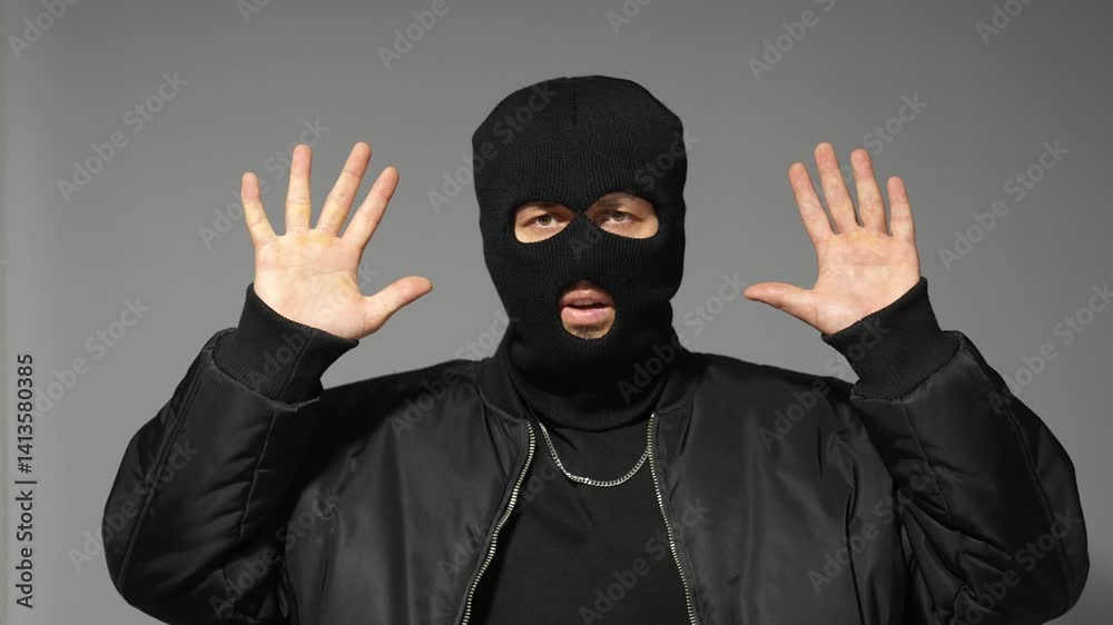 Masked man raising hands in surrender on gray background Masked man raising hands in surrender on gray background