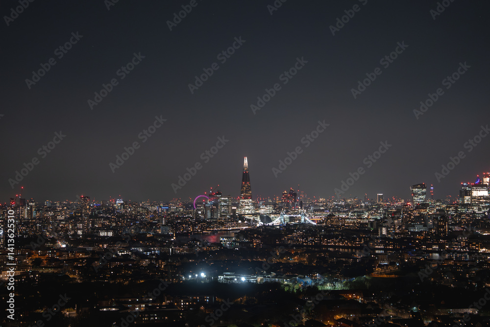 Obraz premium Illuminated Shard skyscraper at night with Tower Bridge spanning the River Thames. The London Eye is visible in the distance under a clear sky.