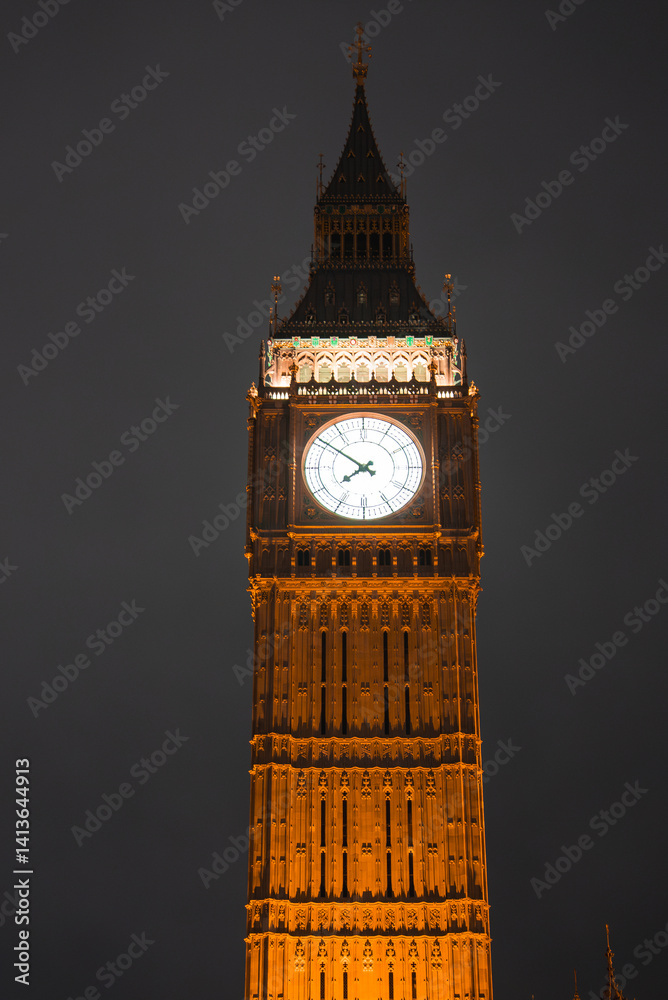 Nighttime view of Elizabeth Tower, also known as Big Ben, in London. The clock face glows brightly, highlighting the tower's intricate architecture.