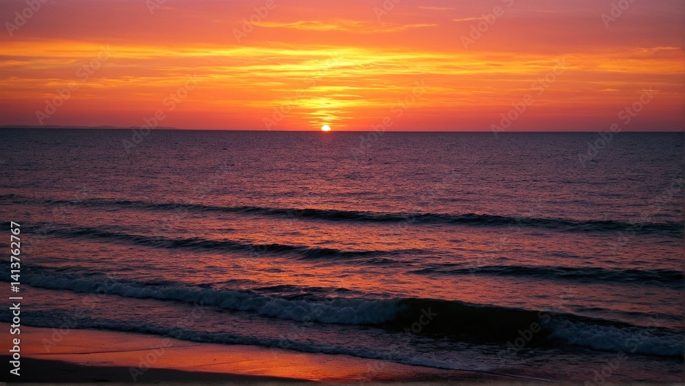 Fototapeta premium Fiery Horizon: A Spectacular Coastal Sunset Painting the Ocean with Vibrant Hues of Orange, Red, and Gold as Gentle Waves Kiss the Shoreline
