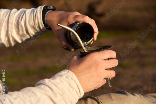 An unrecognizable person pours water from a thermos into a mate, to drink this traditional Argentine beverage.