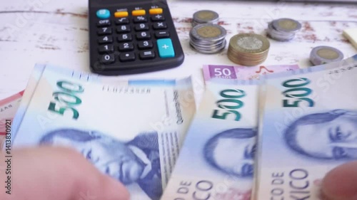 Close-up of a person counting 500 Mexican peso bills, in the background a table with more money and a calculator