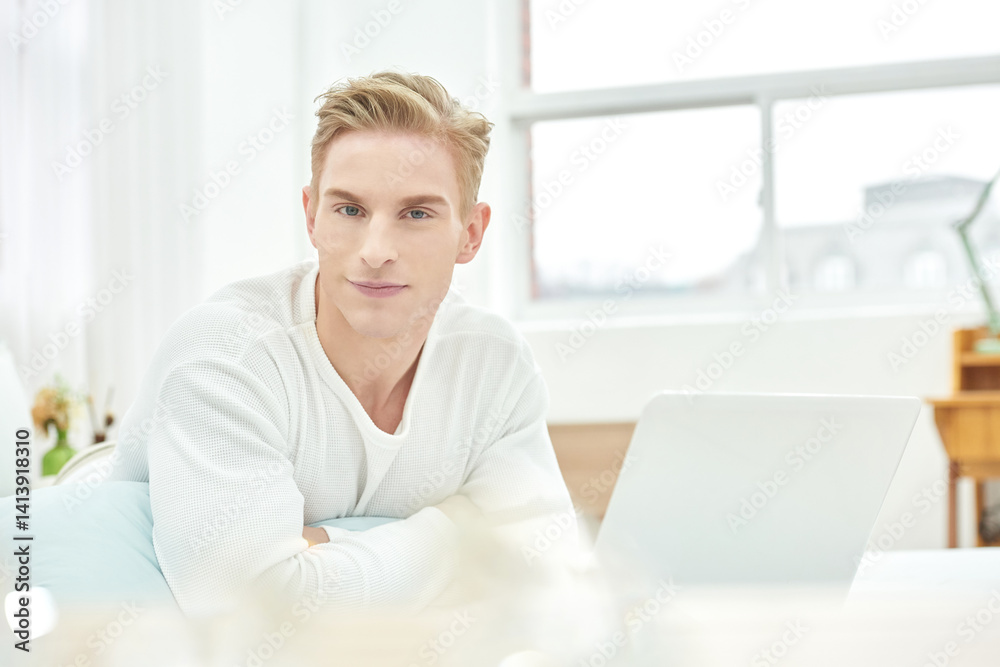 Young Man Relaxing with Laptop in Bright Modern Bedroom Young Man Relaxing with Laptop in Bright Modern Bedroom