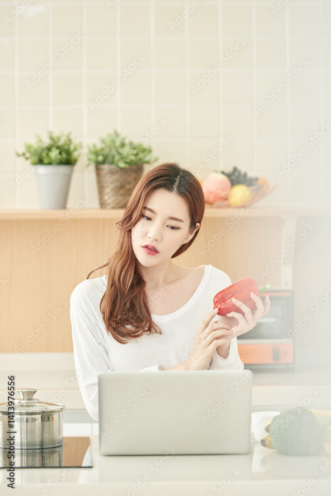 Young Woman Cooking at Home, Searching Recipe Online with Red Bell Pepper Young Woman Cooking at Home, Searching Recipe Online with Red Bell Pepper