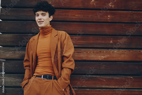Young man in stylish attire against wooden backdrop His expression is confident and relaxed, showcasing modern fashion trends