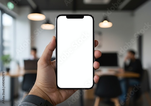 A hand holds a smartphone featuring a blank app interface in a contemporary office setting. Several individuals engage in tasks at desks nearby  creating a productive atmosphere
