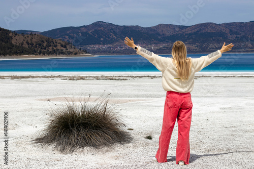 A stylish woman poses playfully beside the vibrant and colorful Salda sign at the stunning Salda Lake Turkey