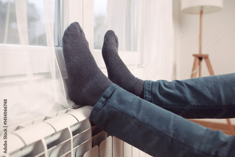 Man's feet with socks on a home heating radiator on a cold winter day outdoors.