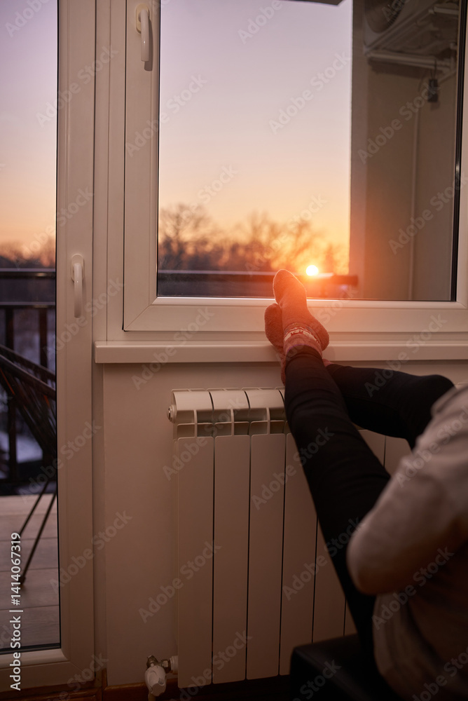 Woman's feet with socks on a home heating radiator on a cold winter day outdoors.