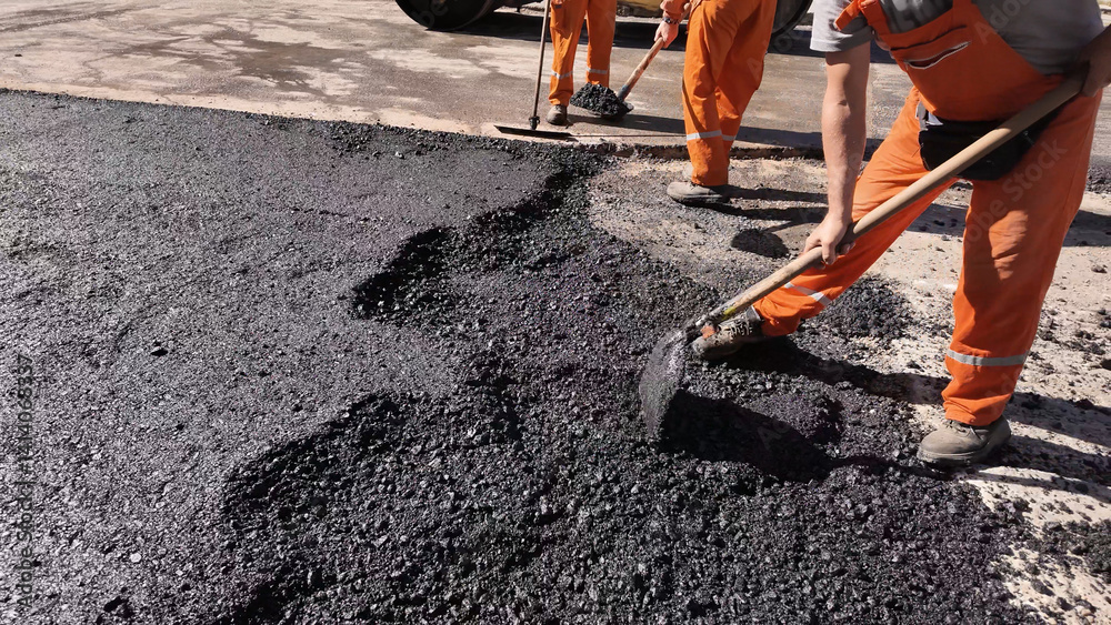 Construction workers working on a new asphalt layer on a public street.