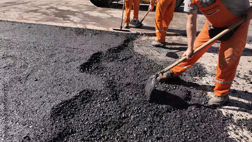 Construction workers working on a new asphalt layer on a public street.
