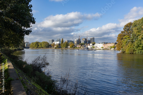 Strand on the Green in Chiswick viewed from Kew Green on banks of River Thames with high rise towers of Brentford in the background