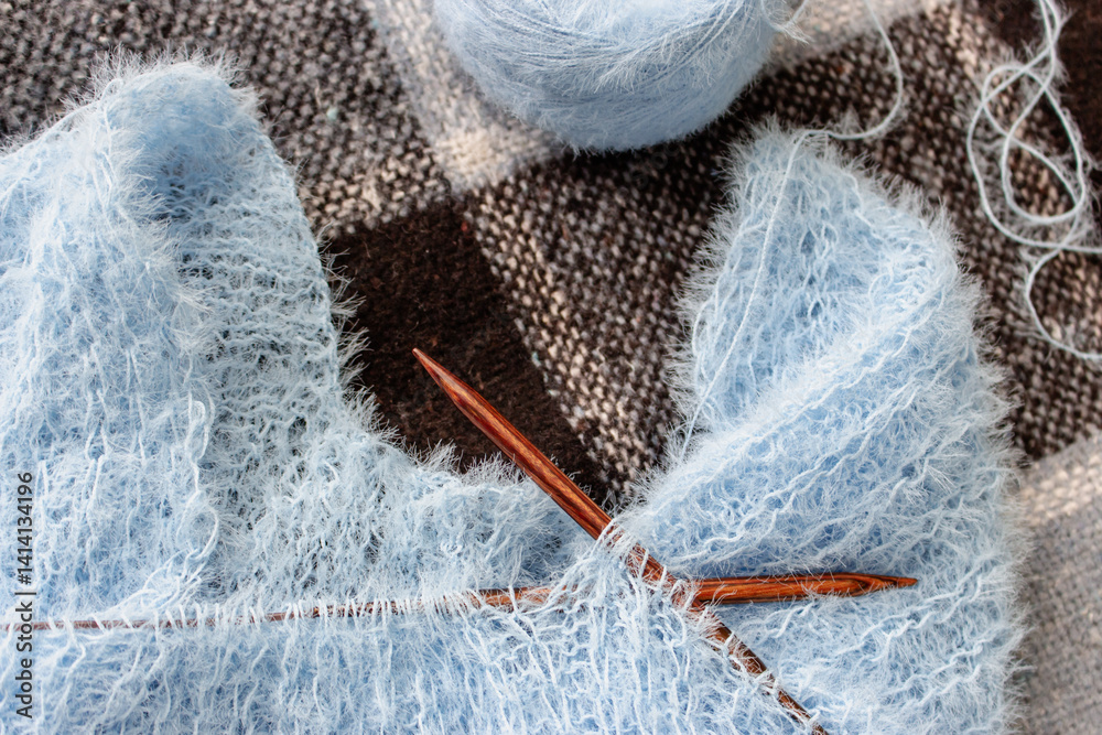 Blue cotton knitting with knitting needles on plaid. Soft blue knitwear with wooden circle needles. Knitting pattern background. Knitting lifestyle. Cozy hobby. Warm knitwear. Craft product concept