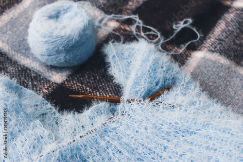 Blue cotton knitting with knitting needles on plaid. Soft blue knitwear with wooden circle needles. Knitting pattern background. Knitting lifestyle. Cozy hobby. Warm knitwear. Craft product concept