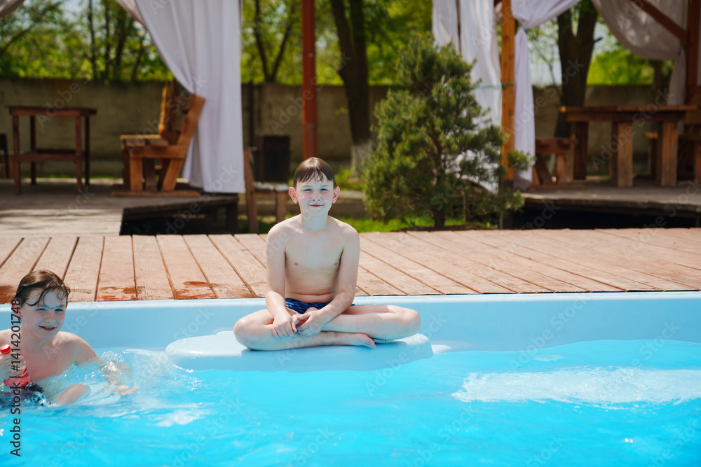 Two boys with a bottle of soda playing and swimming in the pool.