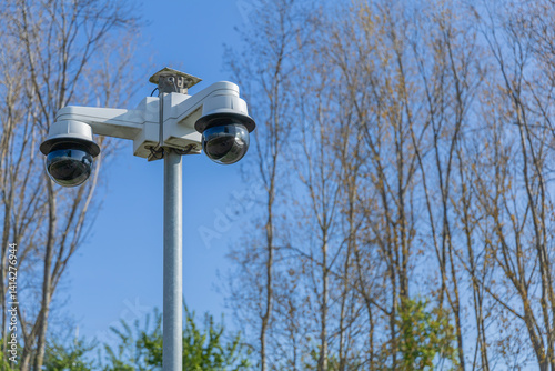 Two security cameras are mounted on a pole, watching over the area under a clear sky
