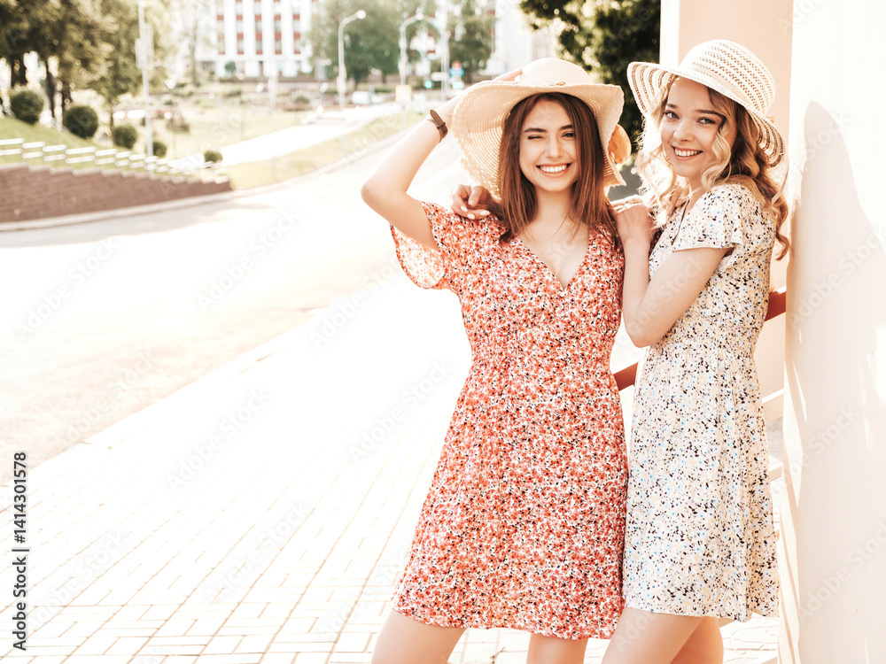 Naklejka premium Two young beautiful smiling hipster girls in trendy summer sundress.Sexy carefree women posing on the street background in hats. Positive models having fun and hugging