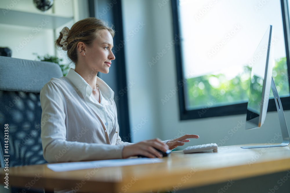 Woman working on computer at a desk in a bright, modern office during daylight hours Woman working on computer at a desk in a bright, modern office during daylight hours
