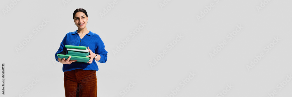 Obraz premium Portrait of smiling woman, librarian holding stack of books against grey studio background. Concept of education,profession, knowledge. Banner. Copy space for ad, text