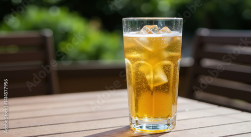 Glass of iced tea with ice cubes on wooden table with blurred green garden background. Refreshing summer drink for outdoor relaxation and patio entertaining
