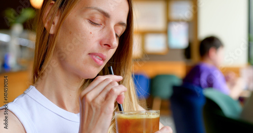 Woman stirs iced coffee with straw while relaxing in a modern cafe