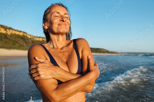 Photography Mature woman embracing herself on the beach during sunset