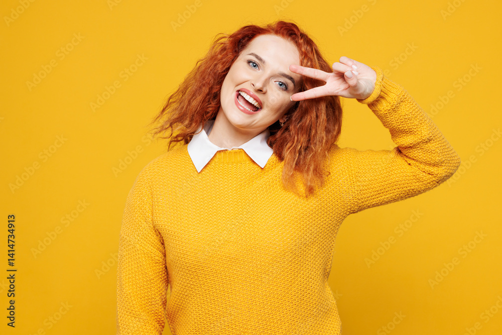 Young smiling happy redhead woman she wears sweater white shirt casual clothes showing cover eye with victory sign look camera isolated on plain yellow background studio portrait. Lifestyle concept. Young smiling happy redhead woman she wears sweater white shirt casual clothes showing cover eye with victory sign look camera isolated on plain yellow background studio portrait. Lifestyle concept.