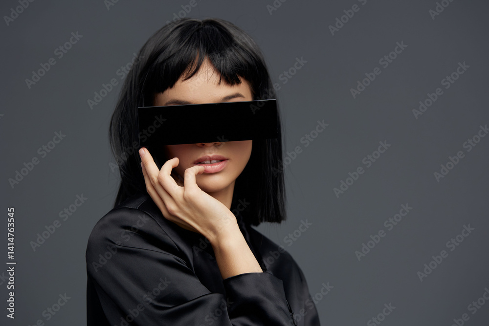 Blackhaired woman with a blindfold covering her eyes, standing against a gray background Blackhaired woman with a blindfold covering her eyes, standing against a gray background