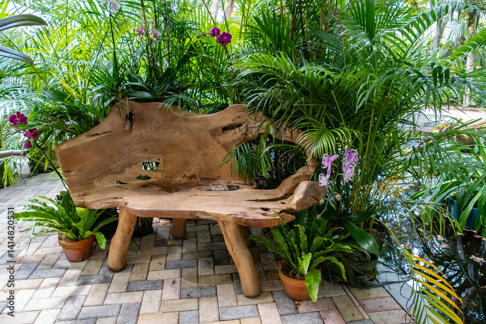 A Carved Wooden Bench Surrounded by Green Tropical Plants and Orchids on a Brick Patio