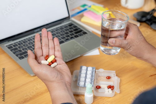 Rear view of a businessman taking pain relief medication after long hours of desk work