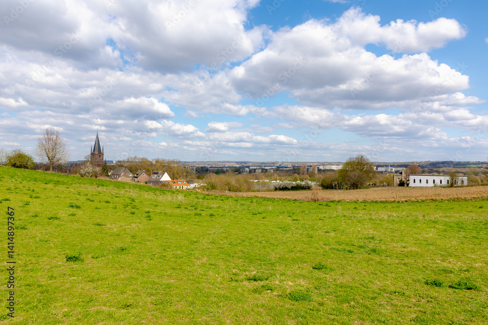 Overview of Maastricht, Terrain of hilly countryside green grass meadow and farmland, Combination with old and new modern buildings, Houses and church on hillside with blue sky, Limburg, Netherlands.