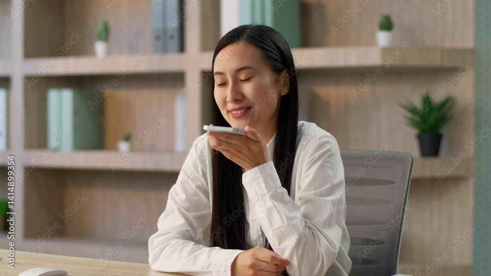 Joyful Chinese businesswoman worker Korean Japanese business woman female manager using mobile phone online app call talking smartphone speakerphone recording voice recognition message send SMS indoor
