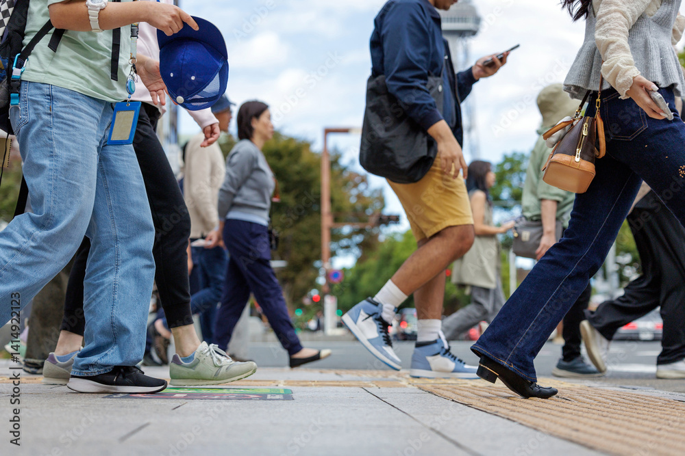 Obraz premium Crowd of casually dressed people head across a busy inner city intersection. Their casual manner is indicative of people out, enjoying weekend activities and leisure time in an urban setting.