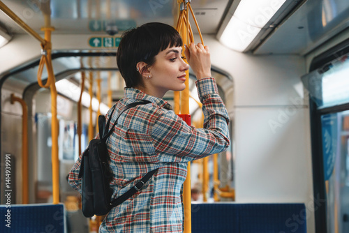 Young woman enjoying a quiet ride on a public transit train while holding onto a pole in an urban setting during midday