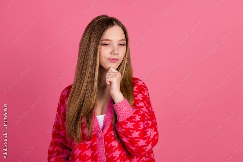 Charming young girl posing with thoughtful expression in casual red cardigan against a pink background Charming young girl posing with thoughtful expression in casual red cardigan against a pink background