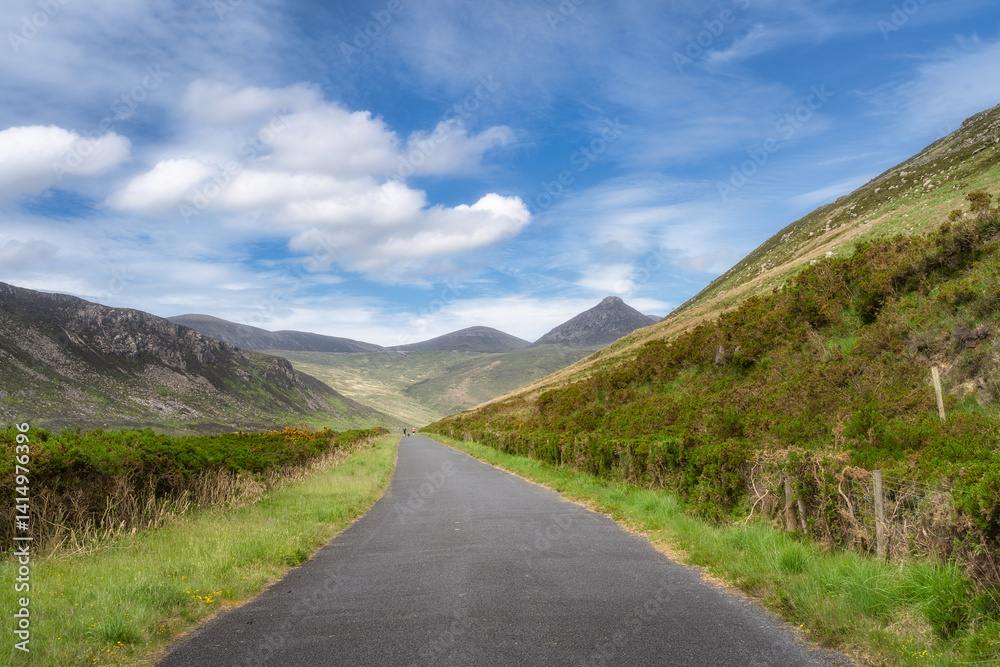 A scenic road winds through lush hills and majestic Mourn Mountains under a clear sky, perfect for nature lovers and adventure seekers looking for exploration, Newry, Northern Ireland